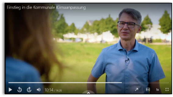  Screenshot aus einem Filmspot zur Anpassung, Zwei Menschen unterhalten sich über die Grünfläche und deren Beitrag zur Klimaanpassung im Hintergrund