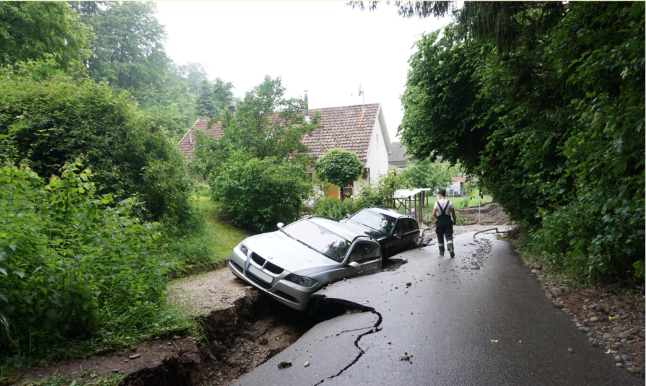Dargestellt ist ein Foto, das zeigt, welche schweren Schäden die starken Regenfälle im Sommer 2021 auch in Baden-Württemberg hinterließen. In Küssaberg führte eine Sturzflut beispielsweise zu aufgerissenen Straßen, so dass dort geparkte Autos in den Grund rutschten.