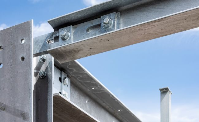 Stahlbauteil mit großer Flexibilität aufgrund spezieller Lochgestaltung. Blickrichtung von unten gegen den blauen Himmel. Die drei Träger sind jeweils im Winkel von 90 Grad zueinander montiert.