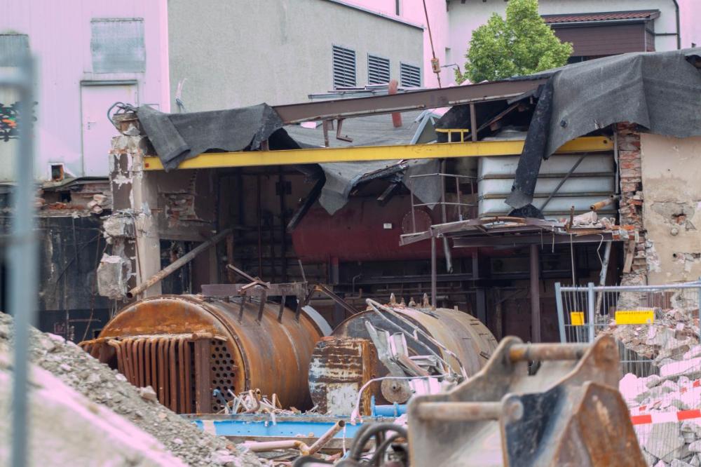 Ein typischer Standort ehemaliger Industrie mit Altlastenrelevanz. Es ist ein Abbruchhaus zu sehen in dem zwei größere und verrostete Kessel stehen. Darum ist Bauschutt.