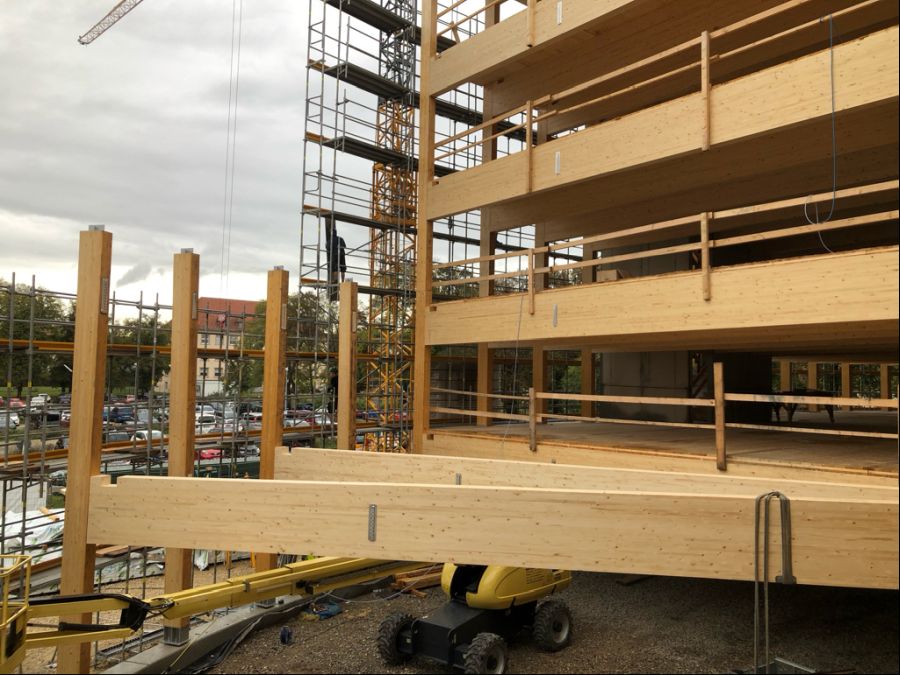 Der Bau des Holzparkhaus befindet sich noch in der Anfangsphase. Man sieht die massiven horuzontalen Holzbalken und im Hintergrund das Gerüst sowie einen Kran.