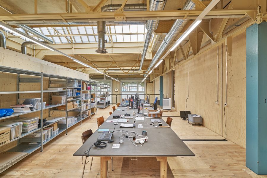 Blick in das Galeriegeschoss. Fußboden Wände und Dachträger aus Holz. Links ein fünfgeschössiges Schwerlastregal, in der Raummitte ein langer, rechteckiger Tisch mit diversem Arbeitsmaterial, unter Anderem ein aufgeklappter Laptop, Steckdosenleiste und Schreibutensilien. Blick in das Galeriegeschoss. Fußboden Wände und Dachträger aus Holz. Links ein fünfgeschössiges Schwerlastregal, in der Raummitte ein langer, rechteckiger Tisch mit diversem Arbeitsmaterial, unter Anderem ein aufgeklappter Laptop, Steckdosenleiste und Schreibutensilien.