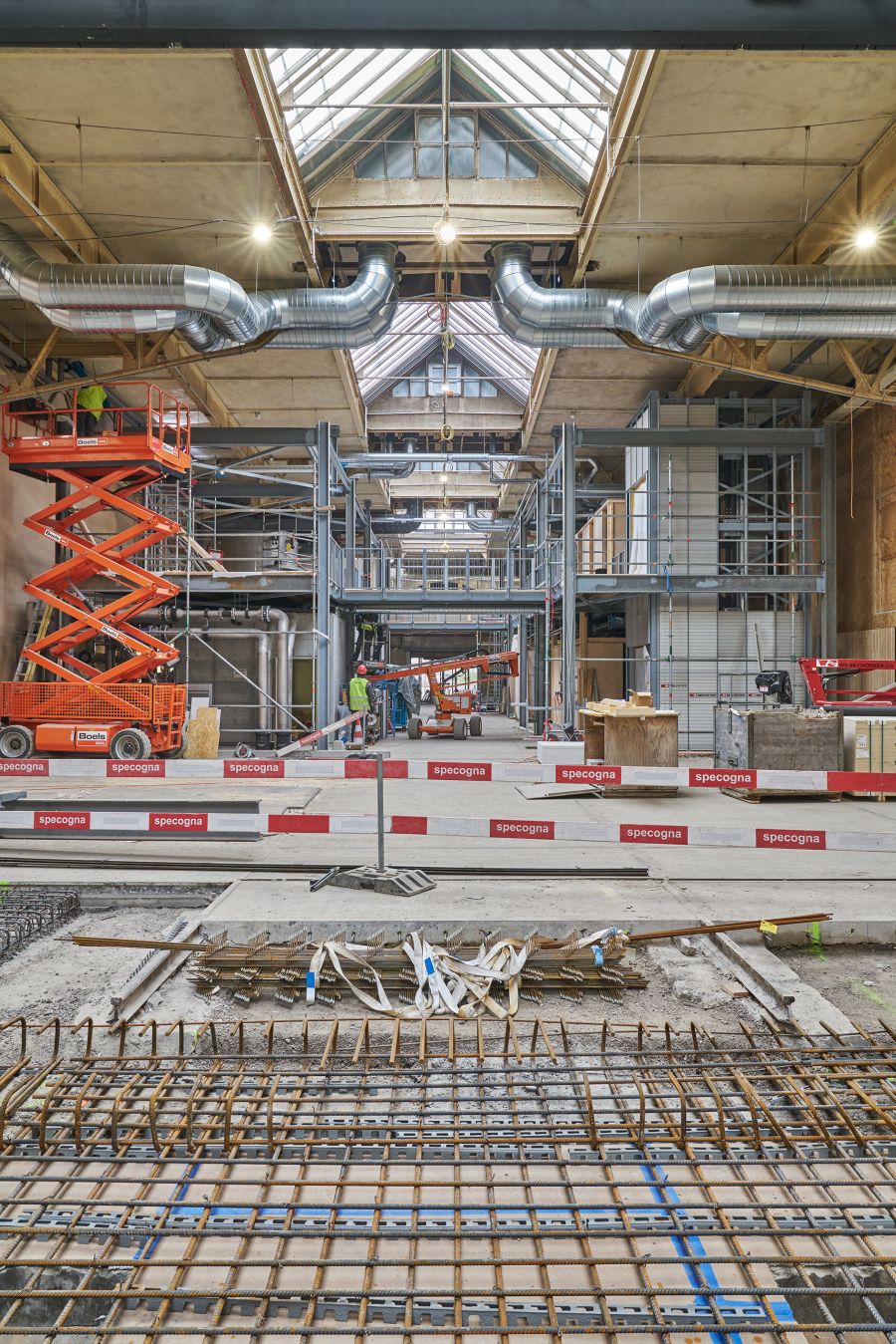 Blick in die Halle. In der Mitte der Halle ist ein Gerüst in Querrichtung aufgestellt, das bis zur Decke reicht. Im Bildvordergrund ist das für den Boden notwendige Armierungsgewebe zu sehen. Der Größte Teil der Bodenfläche ist fertig betoniert. Blick in die Halle. In der Mitte der Halle ist ein Gerüst in Querrichtung aufgestellt, das bis zur Decke reicht. Im Bildvordergrund ist das für den Boden notwendige Armierungsgewebe zu sehen. Der Größte Teil der Bodenfläche ist fertig betoniert.