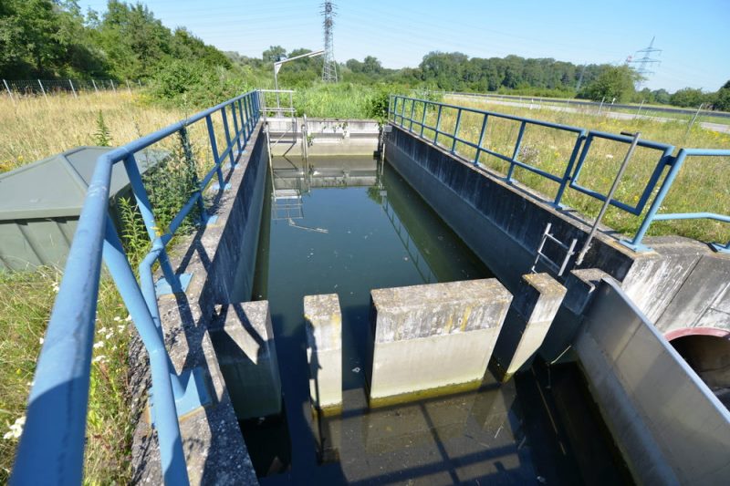 Foto: Teilweise mit Wasser gefülltes Regenklärbecken in sommerlicher Landschaft