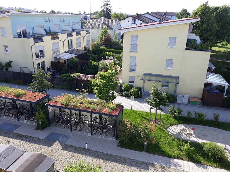 Begrünte urbane Fläche: Flachdach des Fahrradständers ist begrünt, Grünstreifen und wasserdurchlässige Wege.